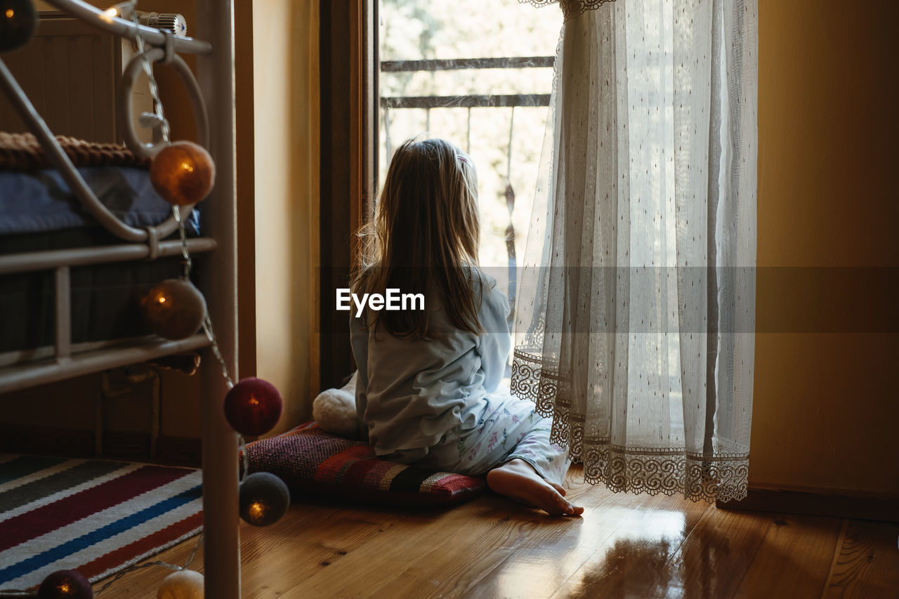 Child sitting on the floor and playing ant home. dreamy sunny mood. girl looking though the window