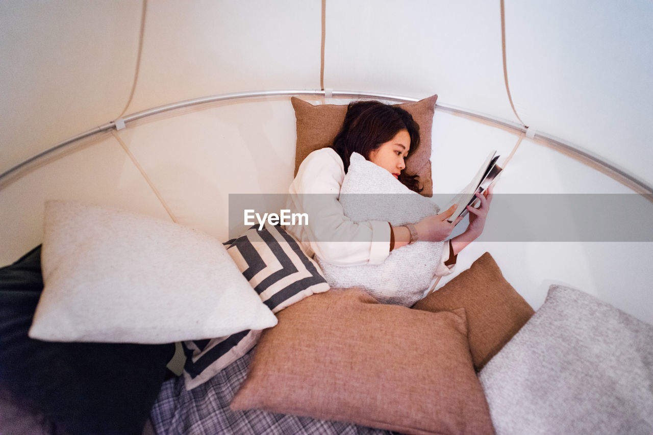 HIGH ANGLE VIEW OF WOMAN USING PHONE WHILE SITTING ON SOFA