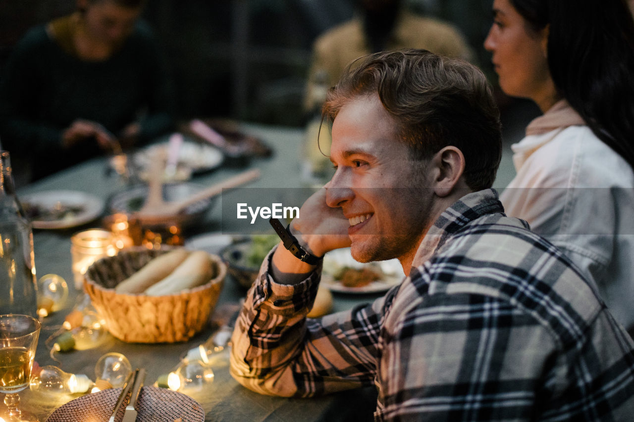 Side view of smiling young man leaning on elbow at dining table during sinner party