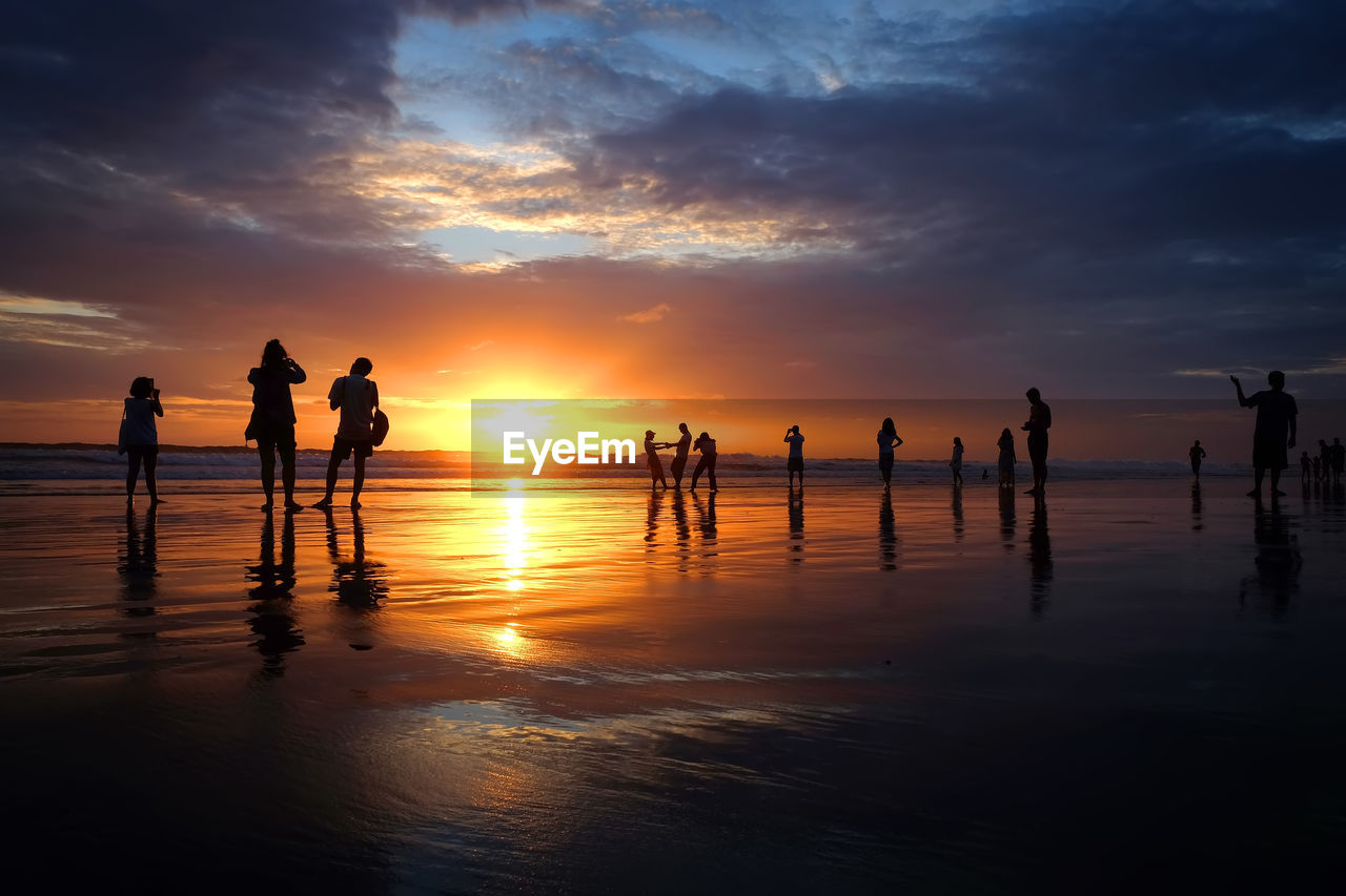 Silhouette people at beach against sky during sunset