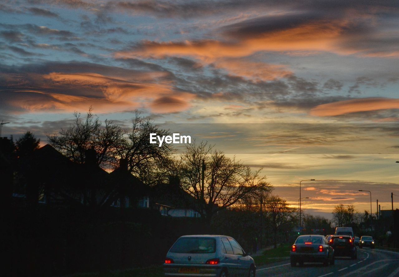 Vehicles on street against cloudy sky during sunset