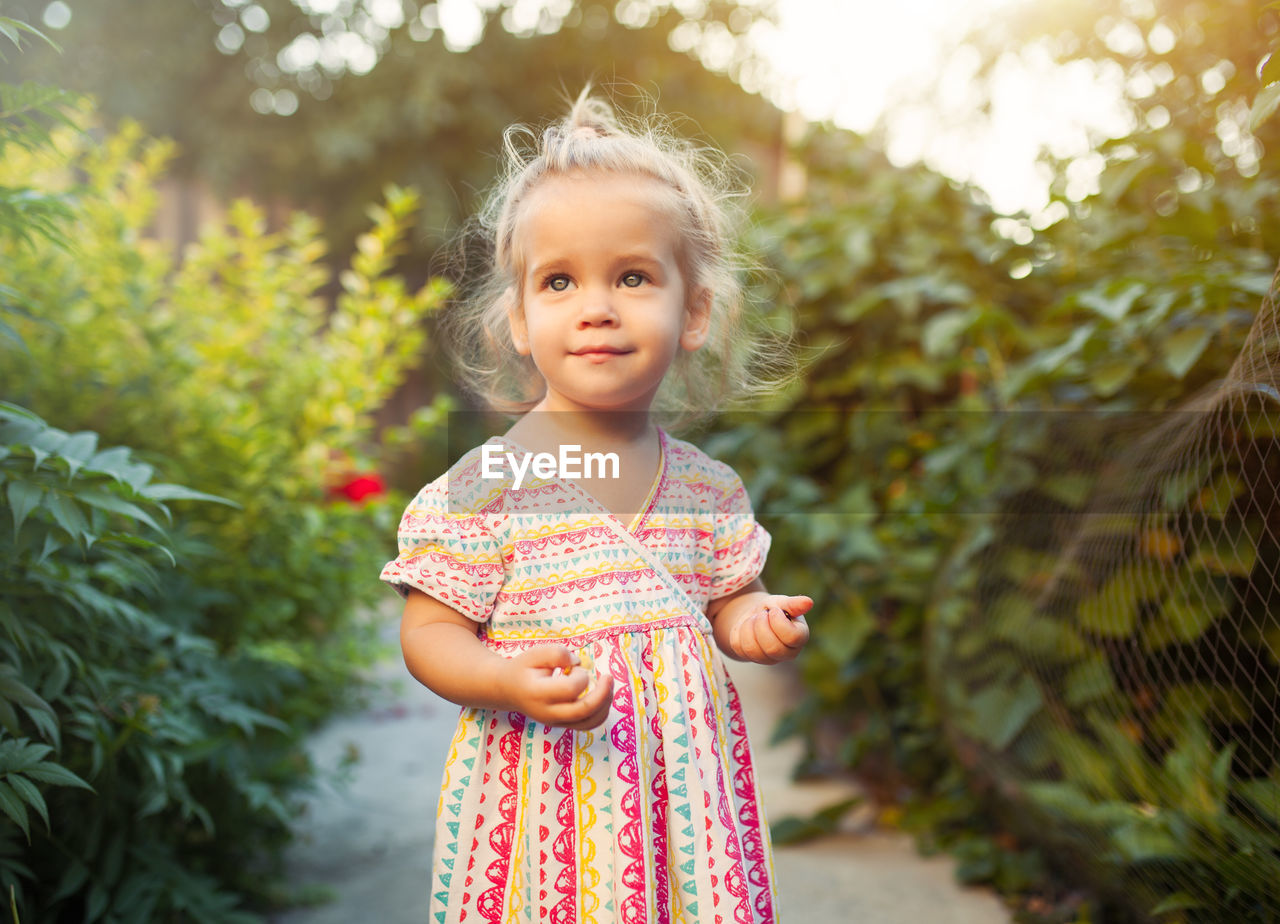 PORTRAIT OF A GIRL STANDING AGAINST PLANTS