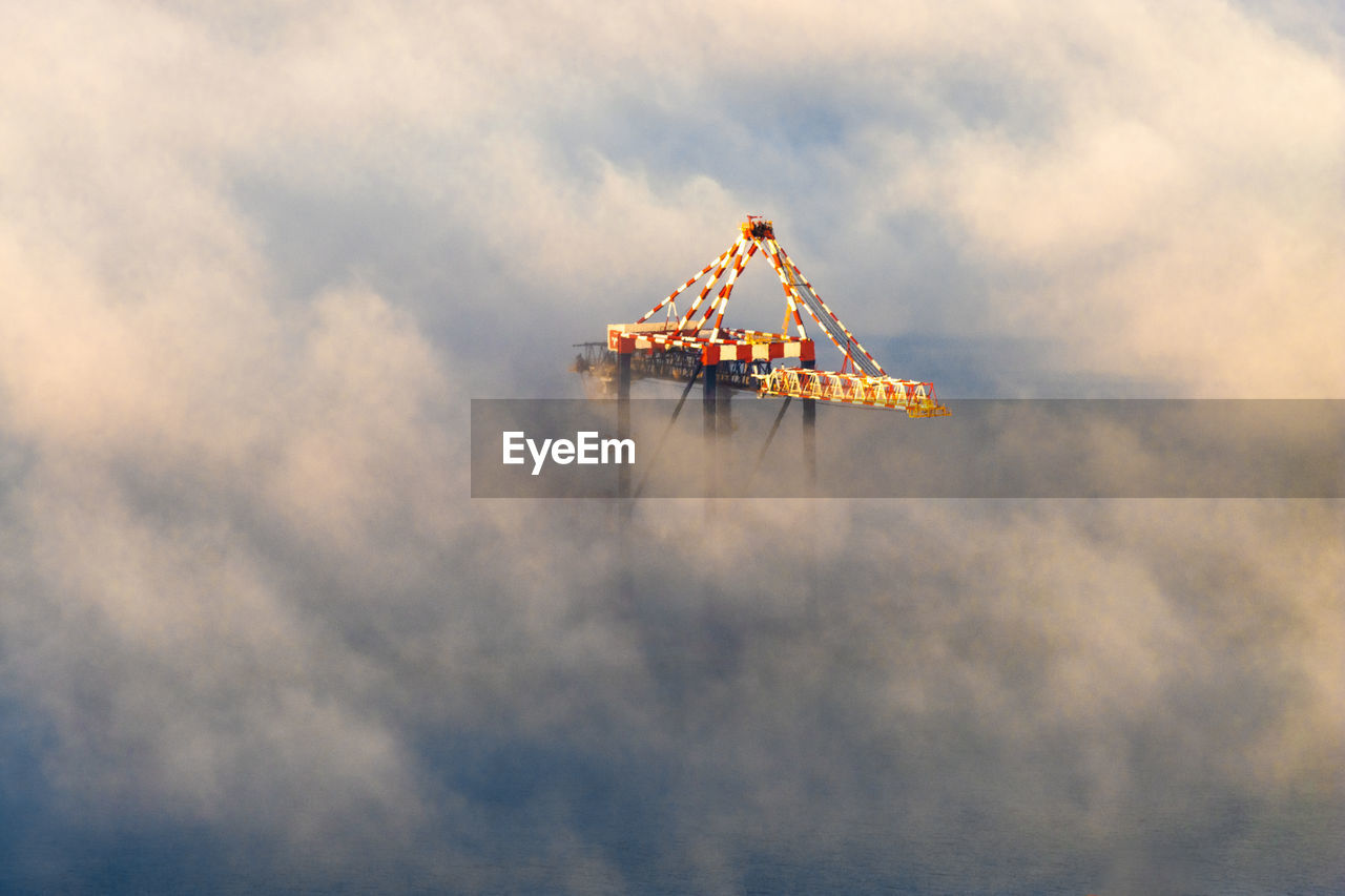 Tip of shipping crane surrounded by mist as sunsets