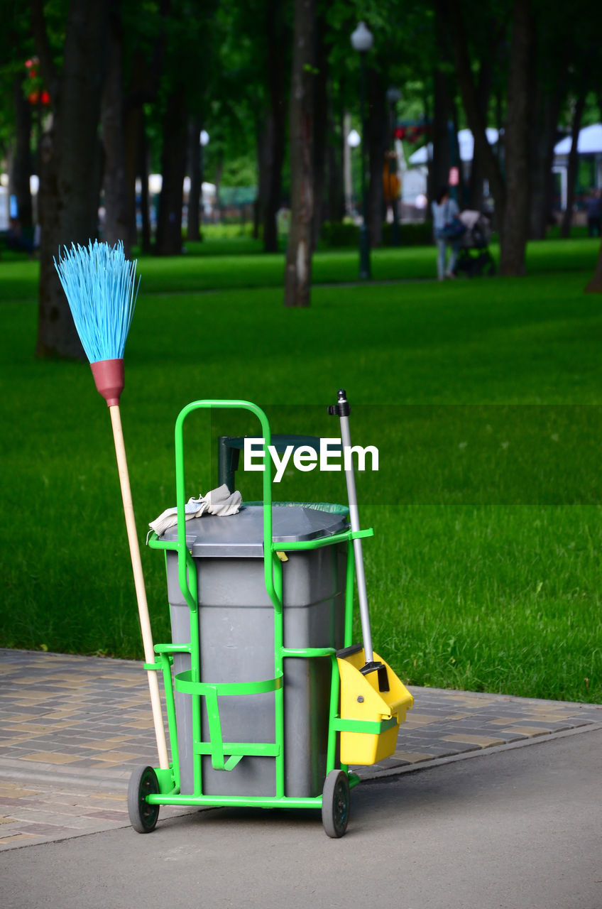 Garbage can with broom against park