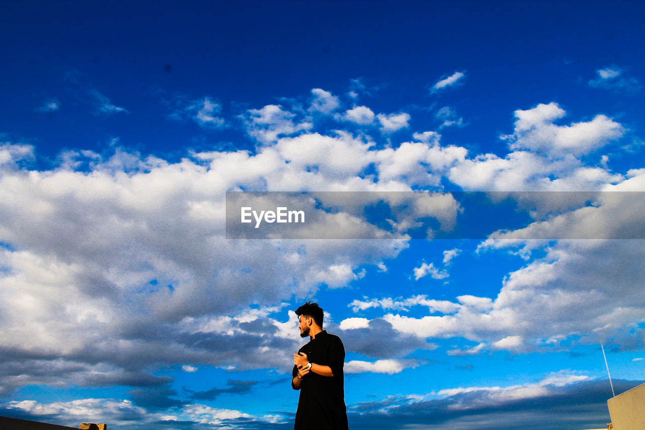 Man standing against blue cloudy sky