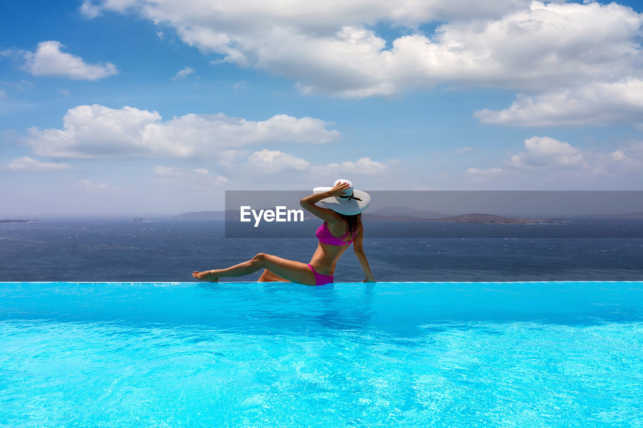 Woman sitting at infinity pool against sea