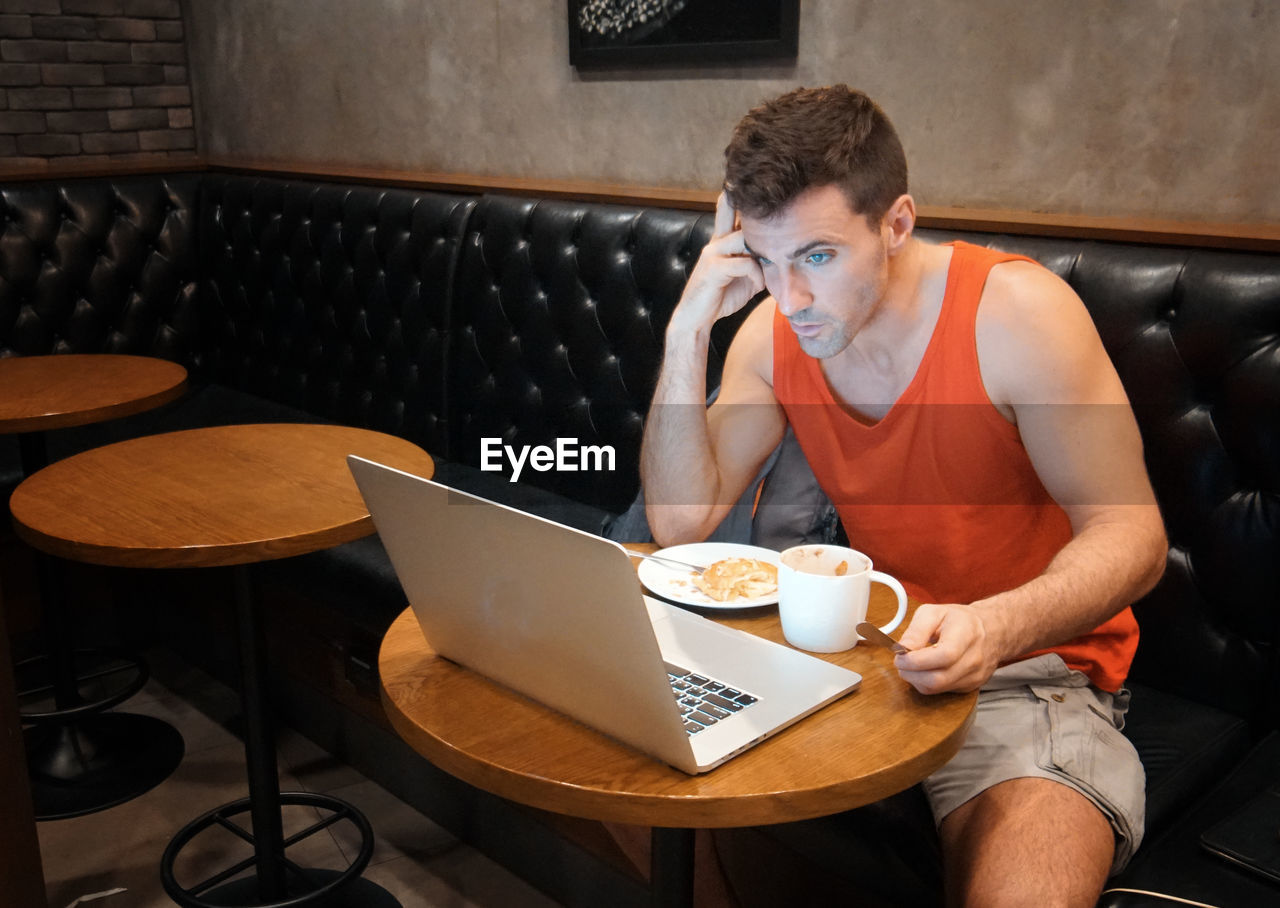 Worried man sitting with coffee and snacks while using laptop at restaurant