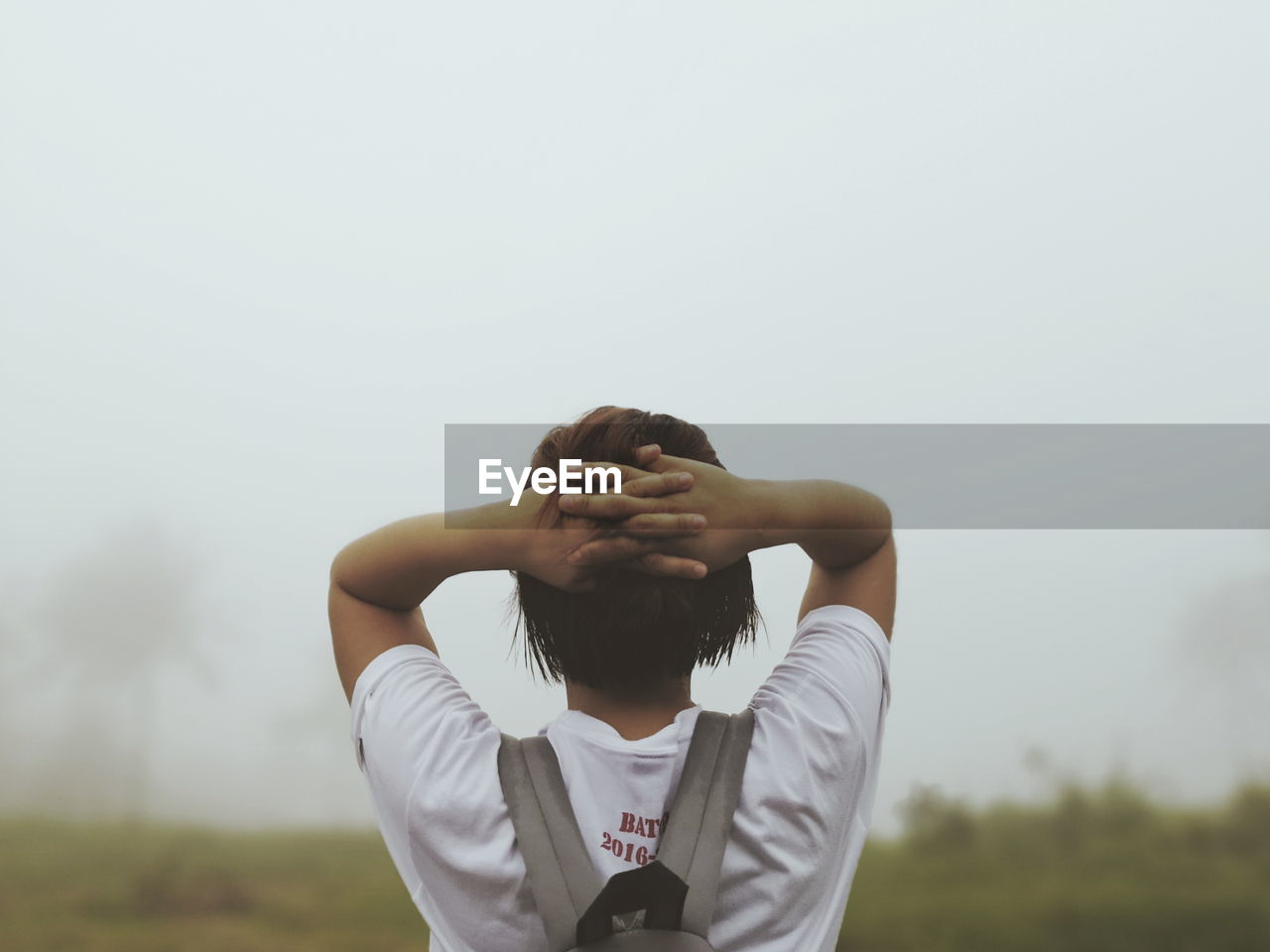 Rear view of woman with hands behind head against sky during foggy weather
