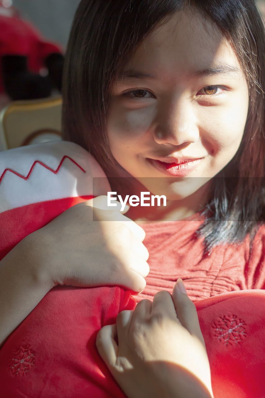 Portrait of beautiful women hugging a doll by a sunny window and a sweet smile looking at the camera