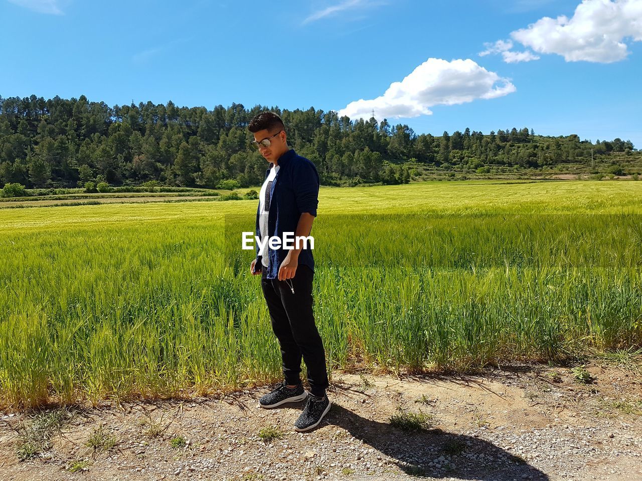 Full length of man standing on roadside by field against sky