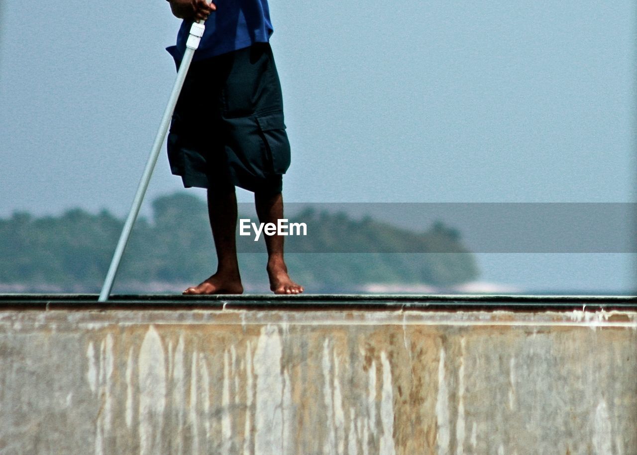 Low section of worker cleaning infinity pool against sky