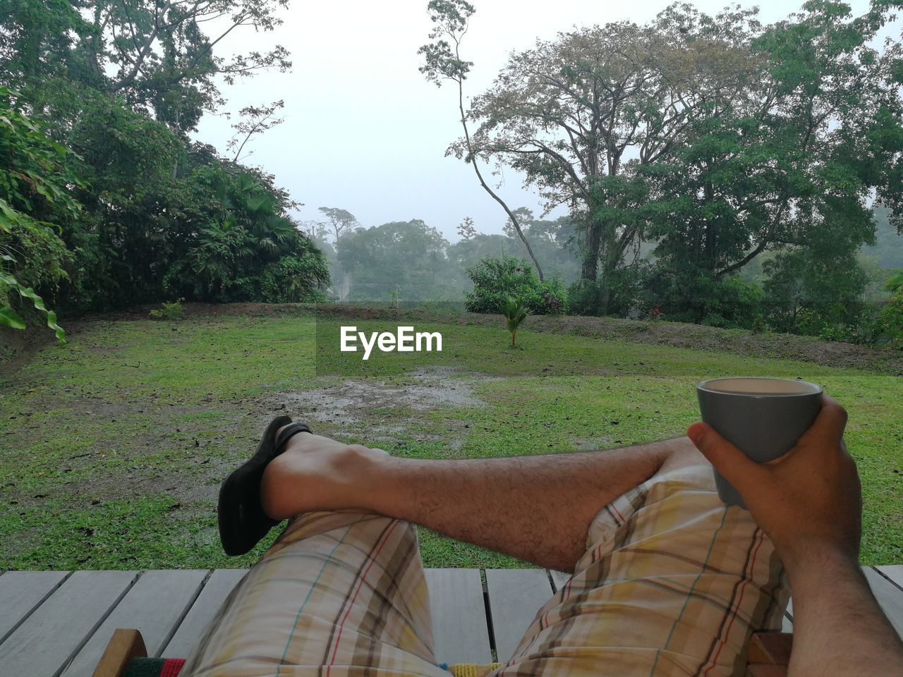 Low section of man holding coffee cup while sitting outdoors