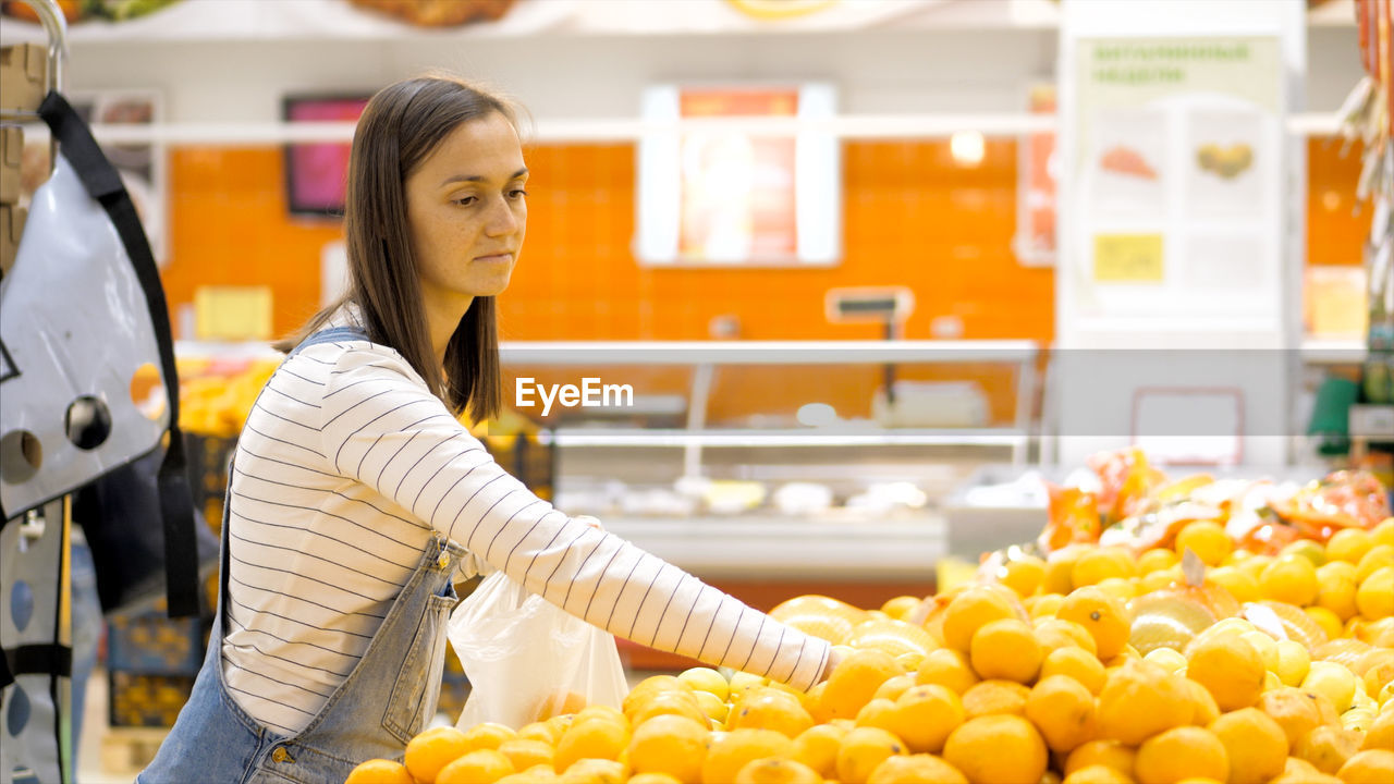 Side view of woman buying oranges in store