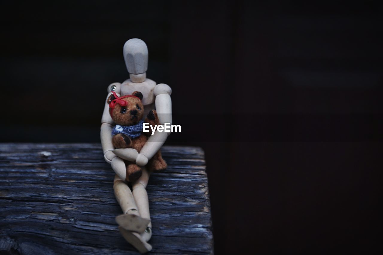 Close-up of figurine with toy on log against black background