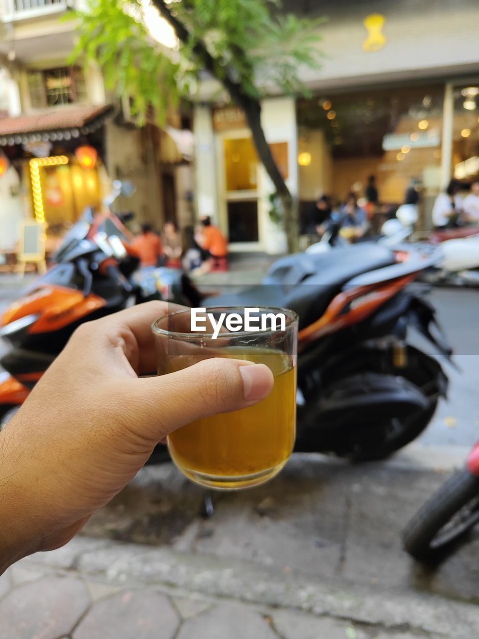 hand, city, street, holding, one person, focus on foreground, architecture, adult, mode of transportation, city life, food and drink, vehicle, yellow, lifestyles, transportation, city street, car, land vehicle, outdoors, leisure activity, drink, day, motor vehicle, wheel, personal perspective, building exterior, travel