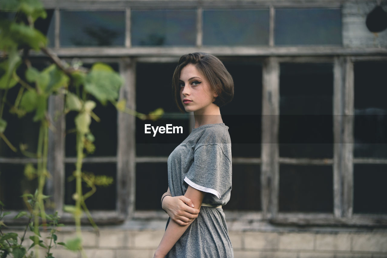 Portrait of young woman standing against windows