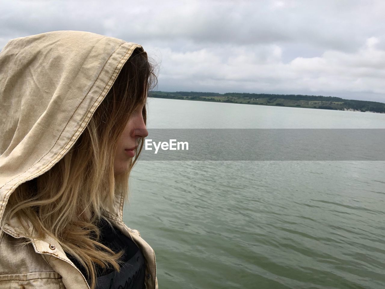 Side view of woman wearing hood standing by lake