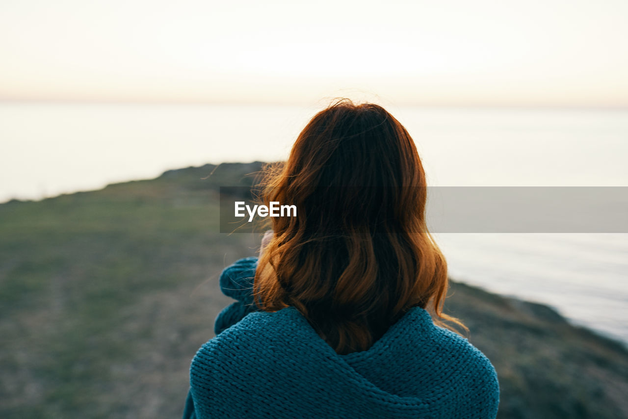 REAR VIEW OF WOMAN LOOKING AT SEA DURING SUNSET