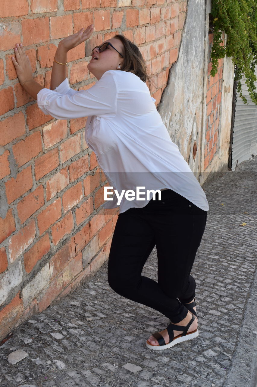 Side view of woman standing against brick wall