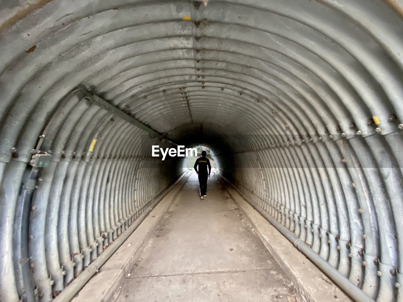 REAR VIEW OF MAN WALKING ON FOOTPATH IN TUNNEL