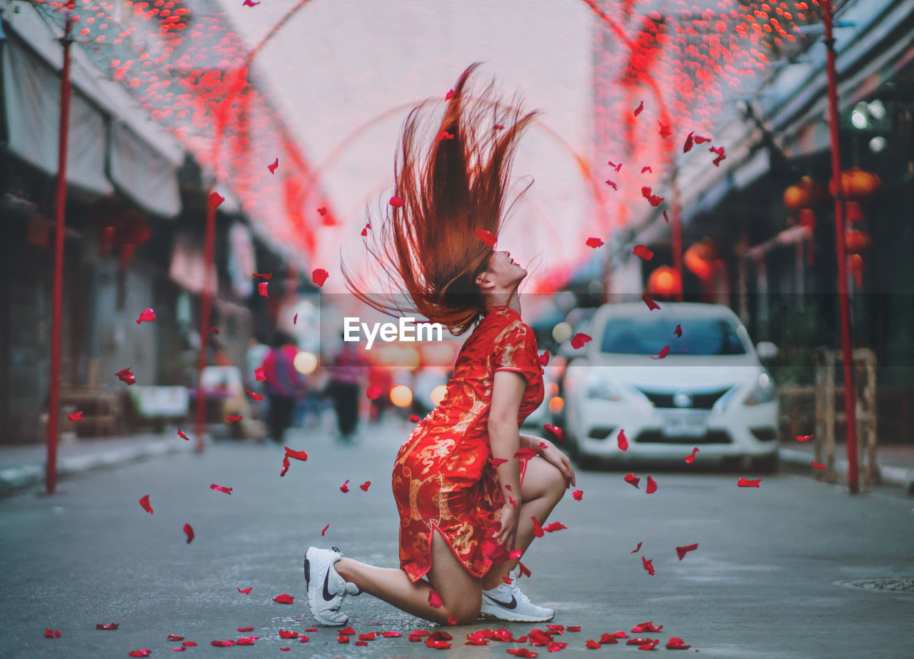 Full length side view of young woman tossing hair on street in city