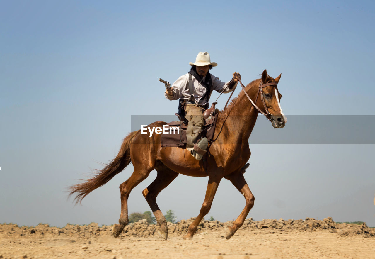 Man with gun riding horse against sky