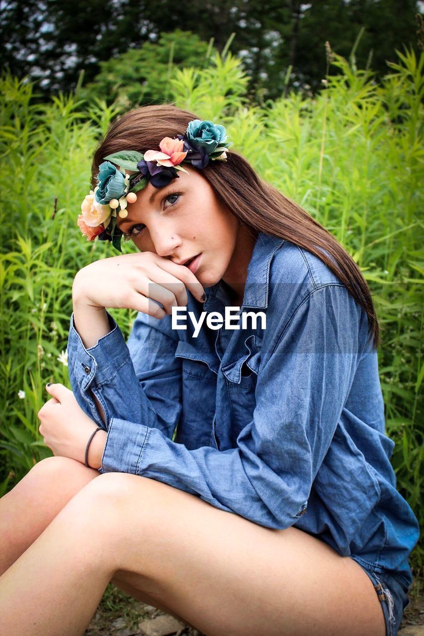 BEAUTIFUL YOUNG WOMAN SITTING ON GRASS AGAINST PLANTS