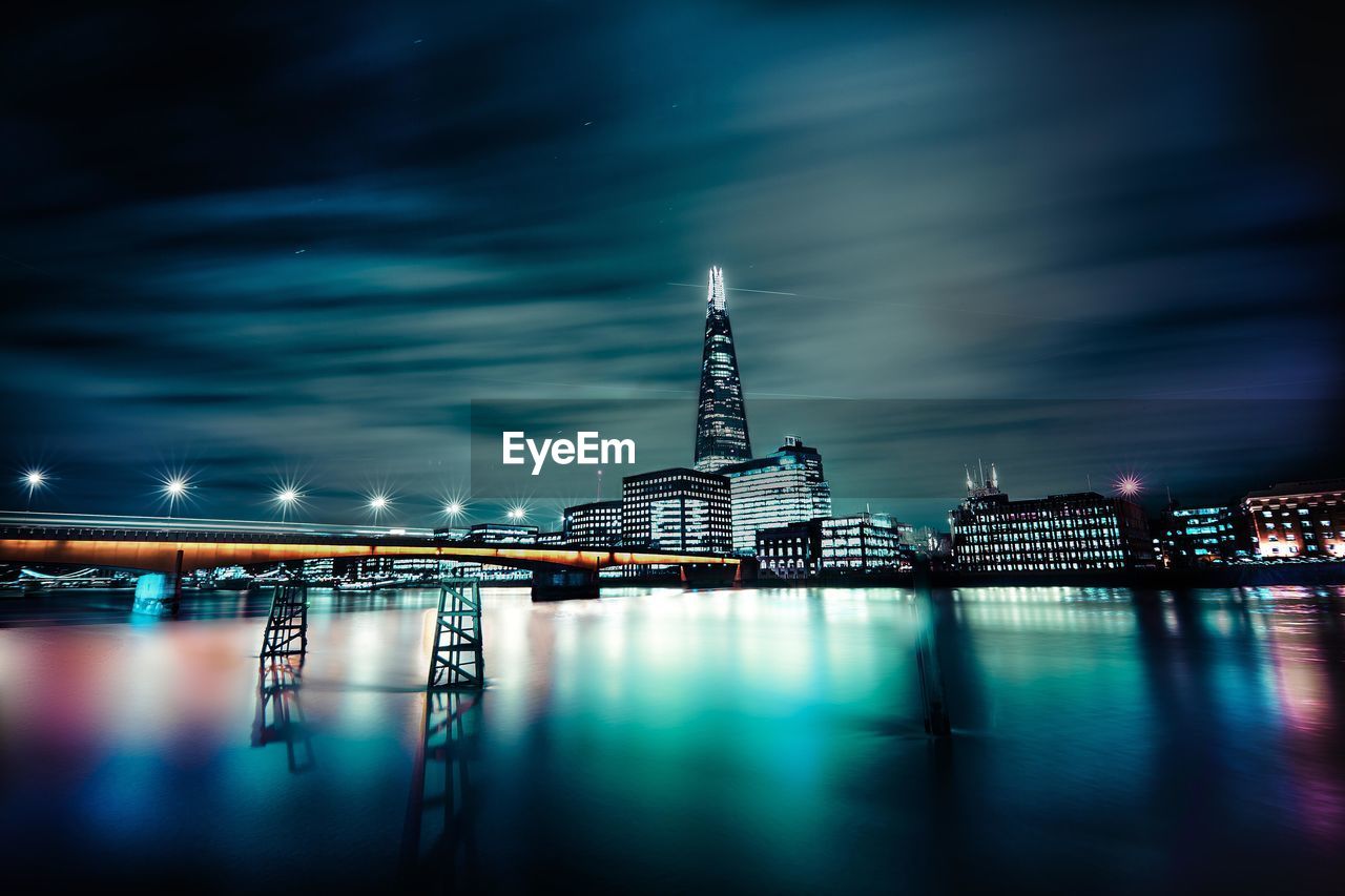 Bridge over thames river with reflection against modern buildings at night