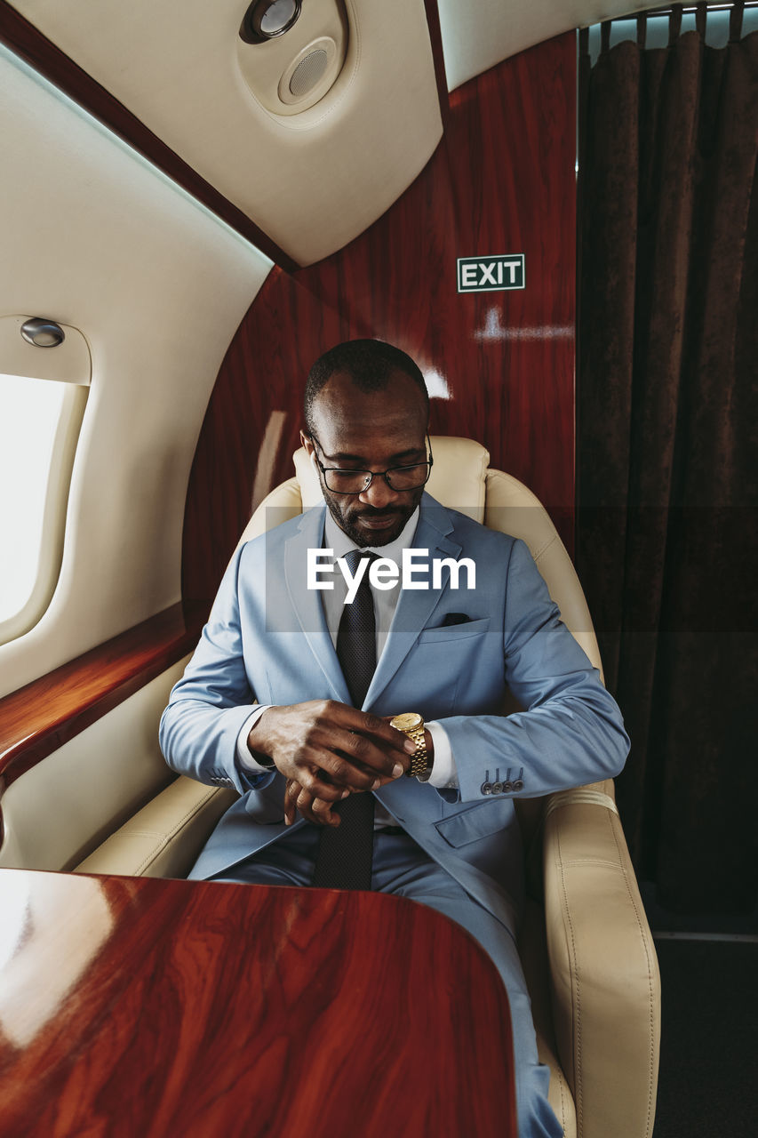 Male entrepreneur checking time on wristwatch while traveling in private jet