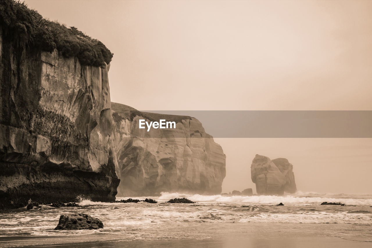 Rock formations by sea against clear sky