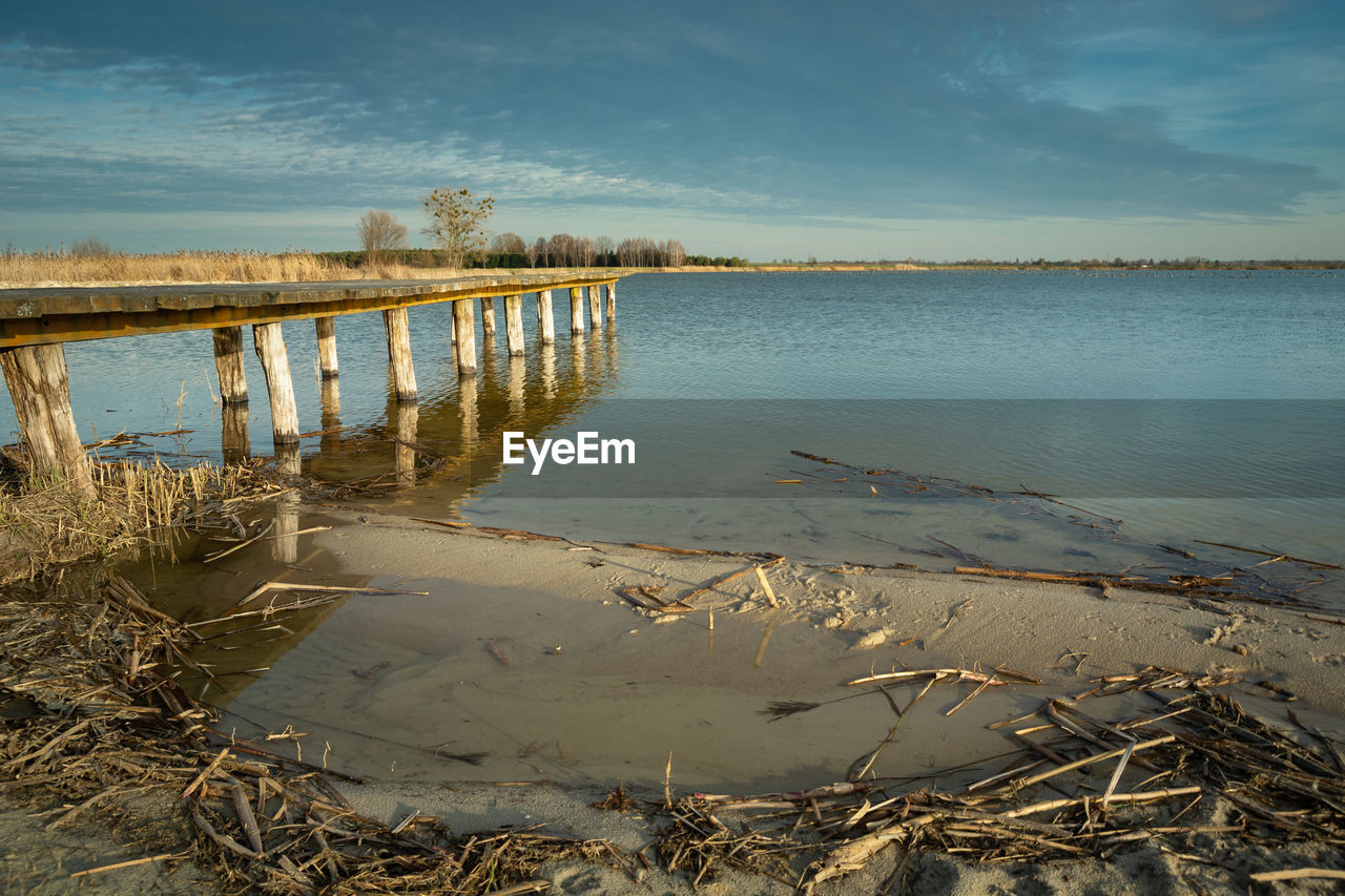 Sandy beach and wooden jetty, evening clouds on a blue sky