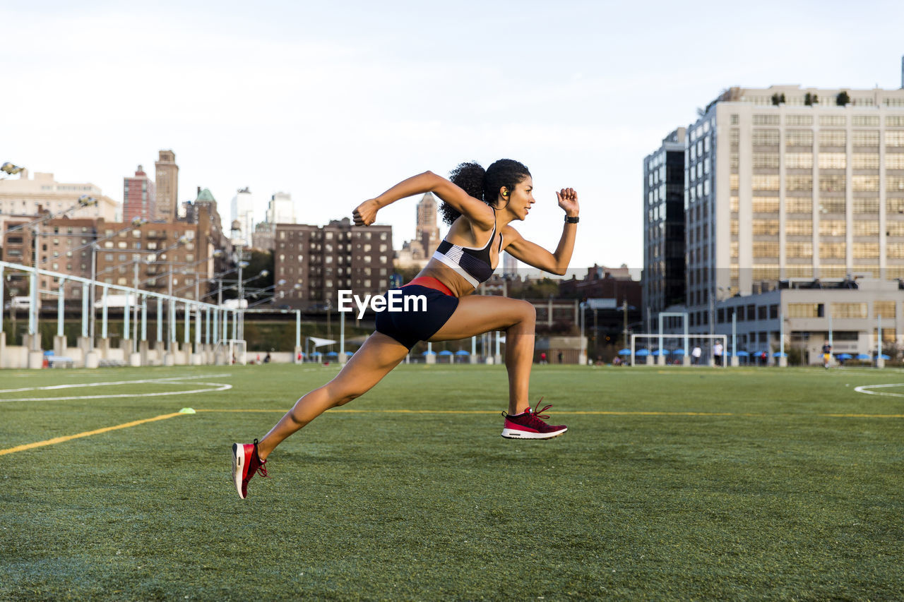 Side view of female athlete running on grassy field against sky