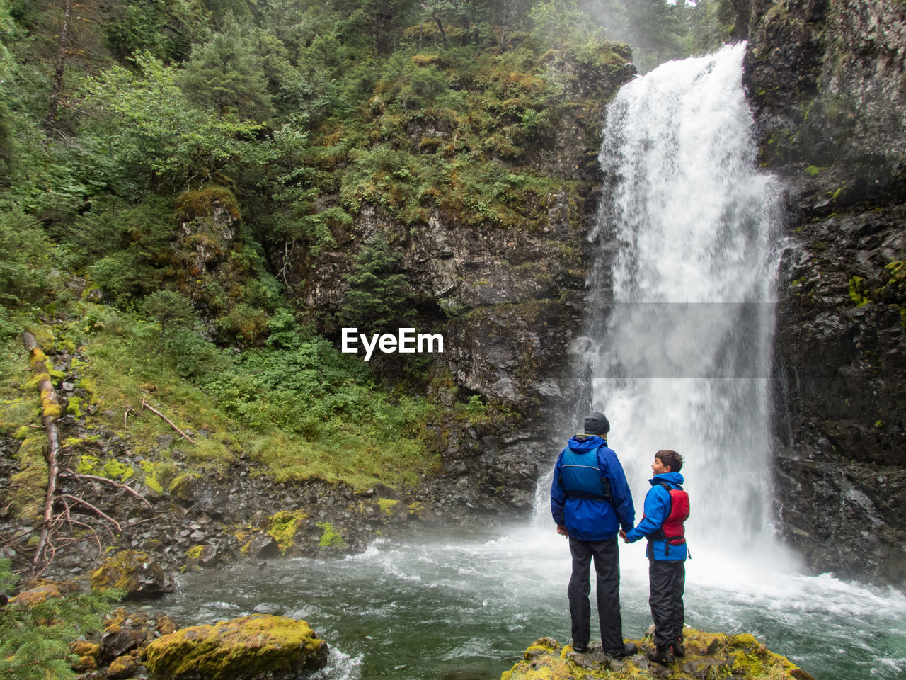 Father and son standing against waterfall in forest