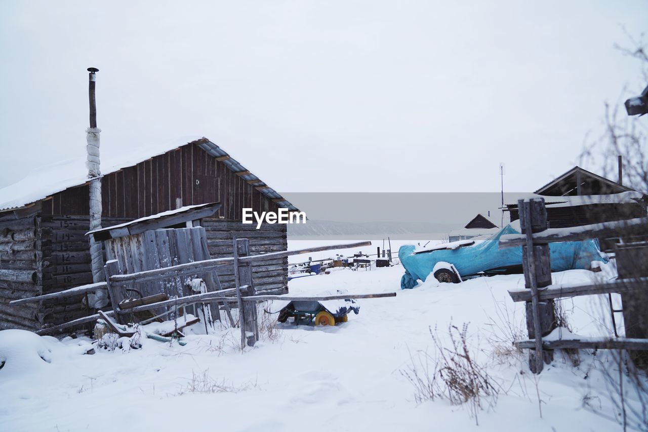 SNOW COVERED HOUSES ON FIELD AGAINST SKY