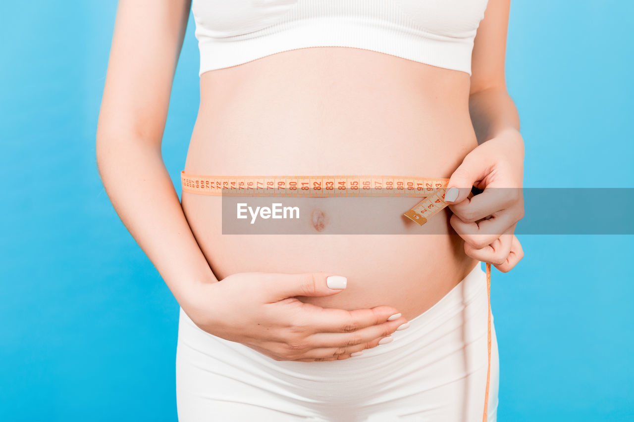 LOW SECTION OF WOMAN STANDING AGAINST BLUE BACKGROUND