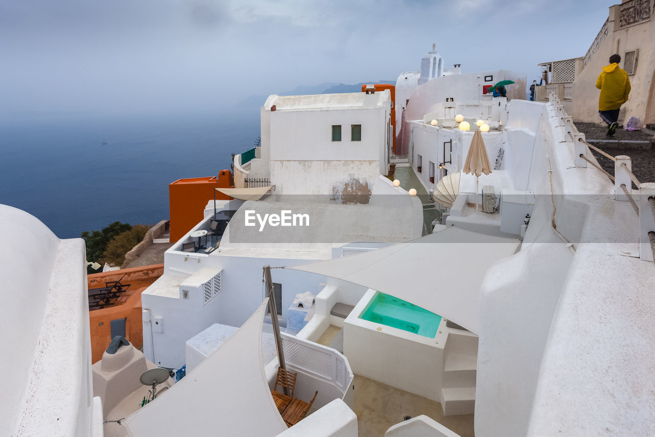 View of colorful houses of oia on a rare rainy day with pool, santorini island, greece