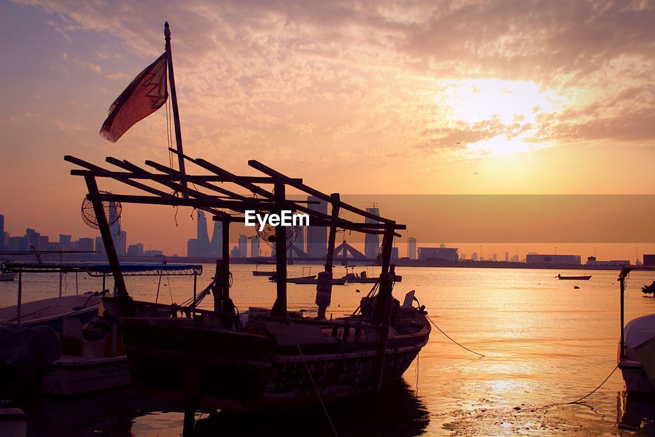 Boats moored in sea against orange sky during sunset