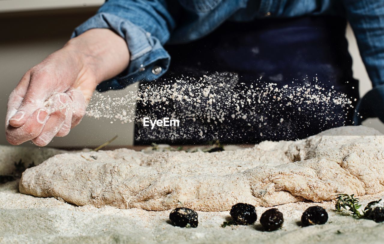 Midsection of person spreading flour on dough in bakery