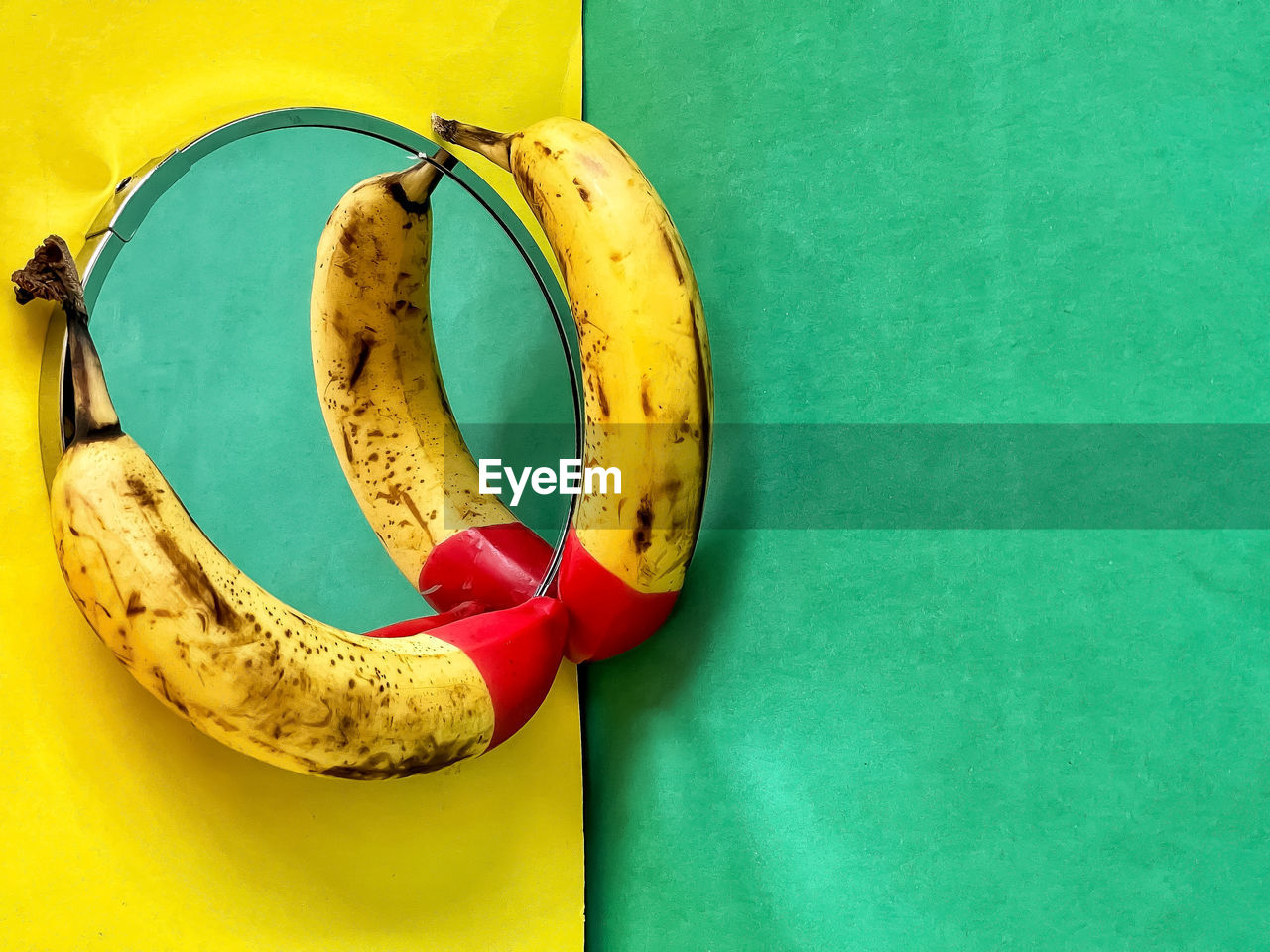 Red tipped bananas on mirror on yellow and green background.