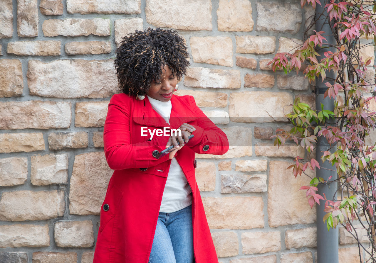 Serious african american woman looks impatiently at her wrist watch near house