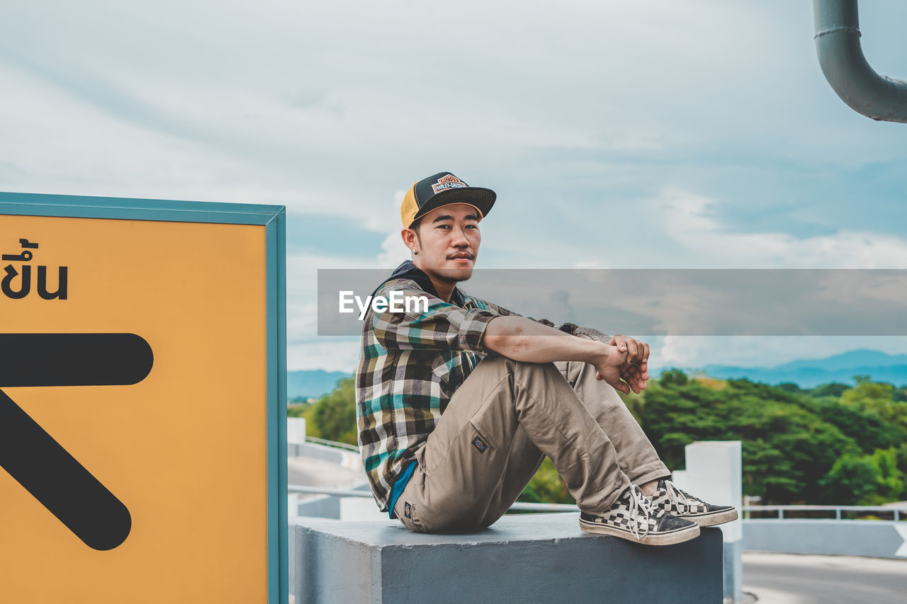 Full length of young man sitting against sky