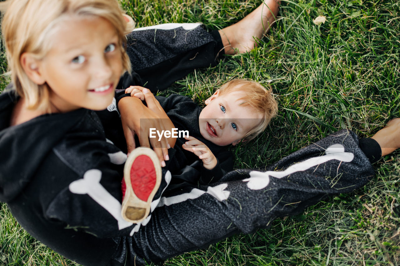 A girl in a hat and a skeleton costume plays with her younger brother on the grass in the garden. 