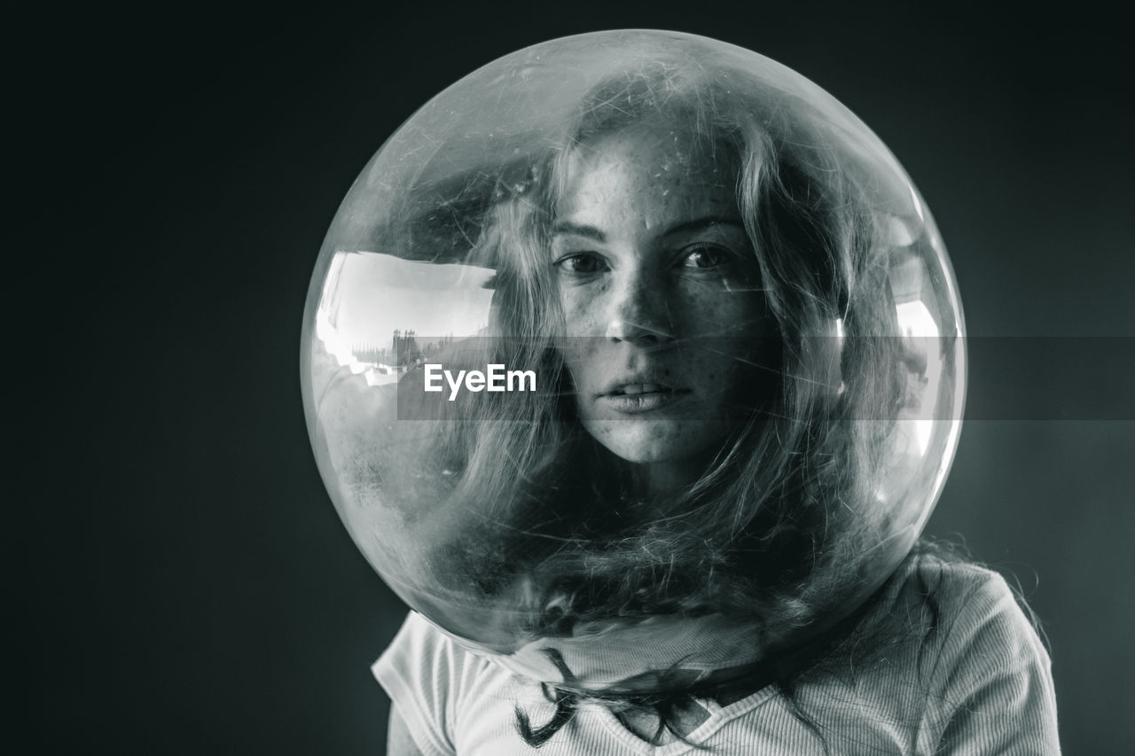 Young woman wearing glass container against black background