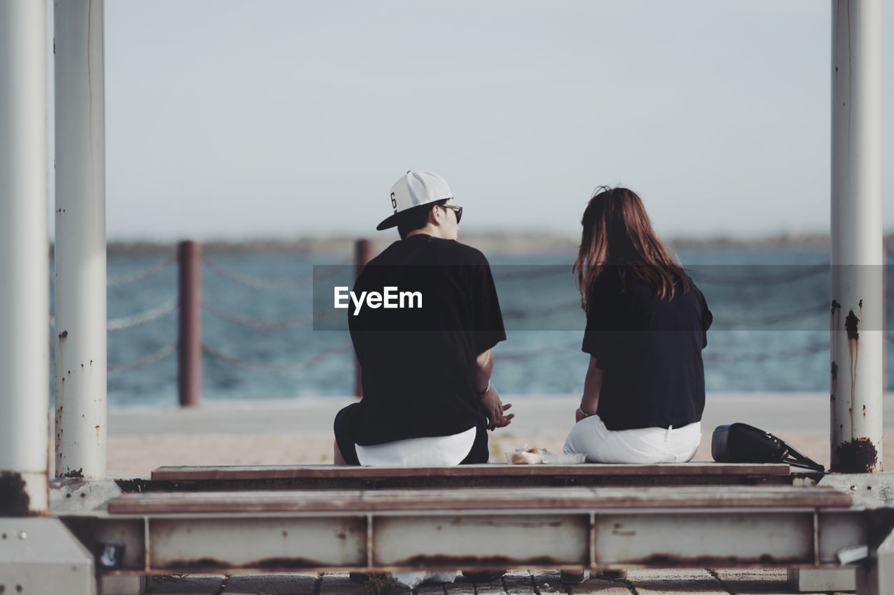 REAR VIEW OF TWO PEOPLE LOOKING AT SEA