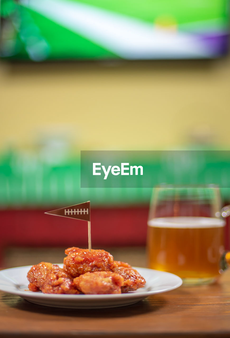 Plate of spicy bbq boneless chicken wings and large glass mug of beer ready for football game