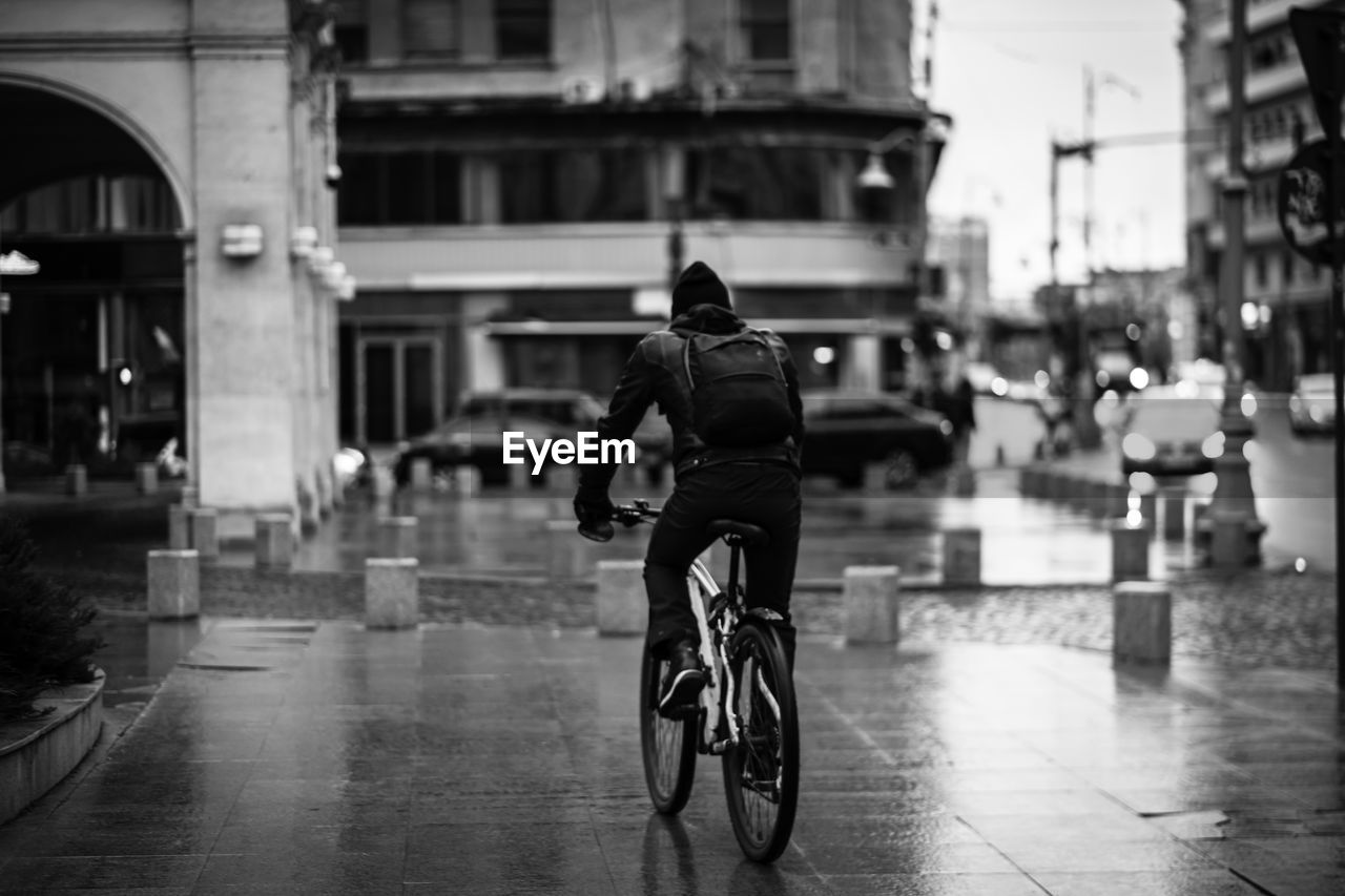 REAR VIEW OF MAN CYCLING ON STREET