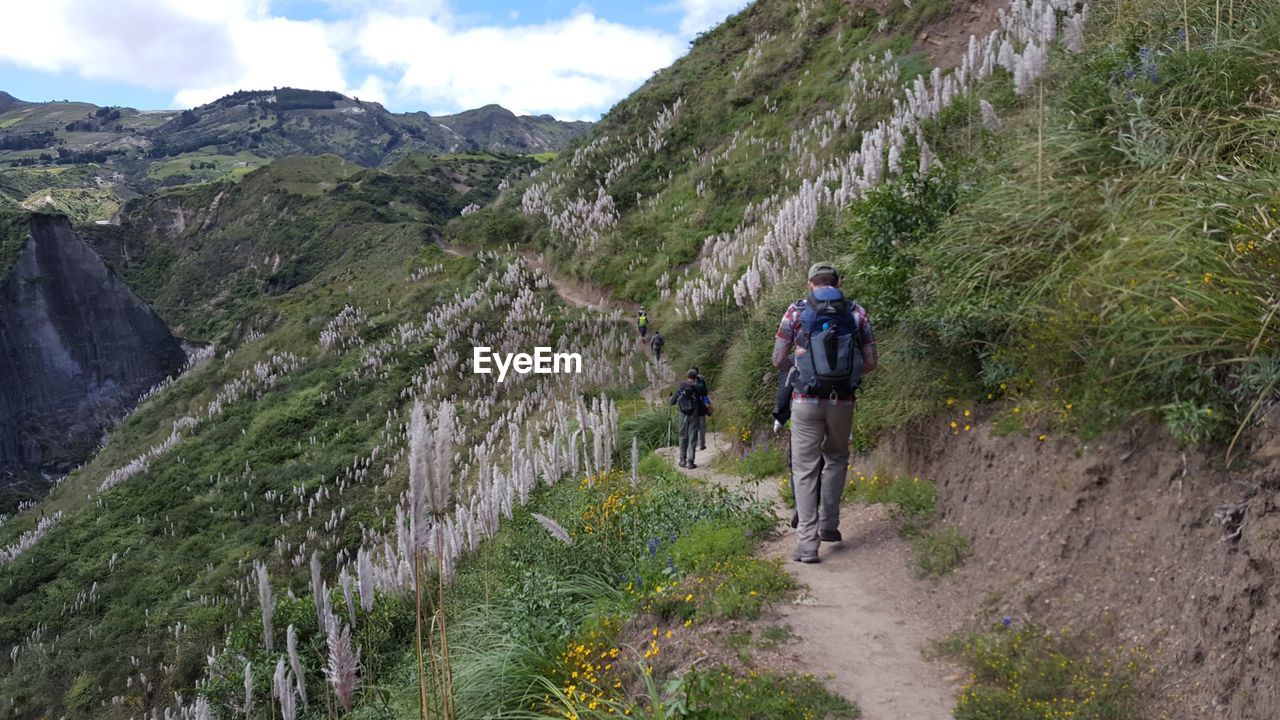 REAR VIEW OF HIKERS WALKING ON MOUNTAIN