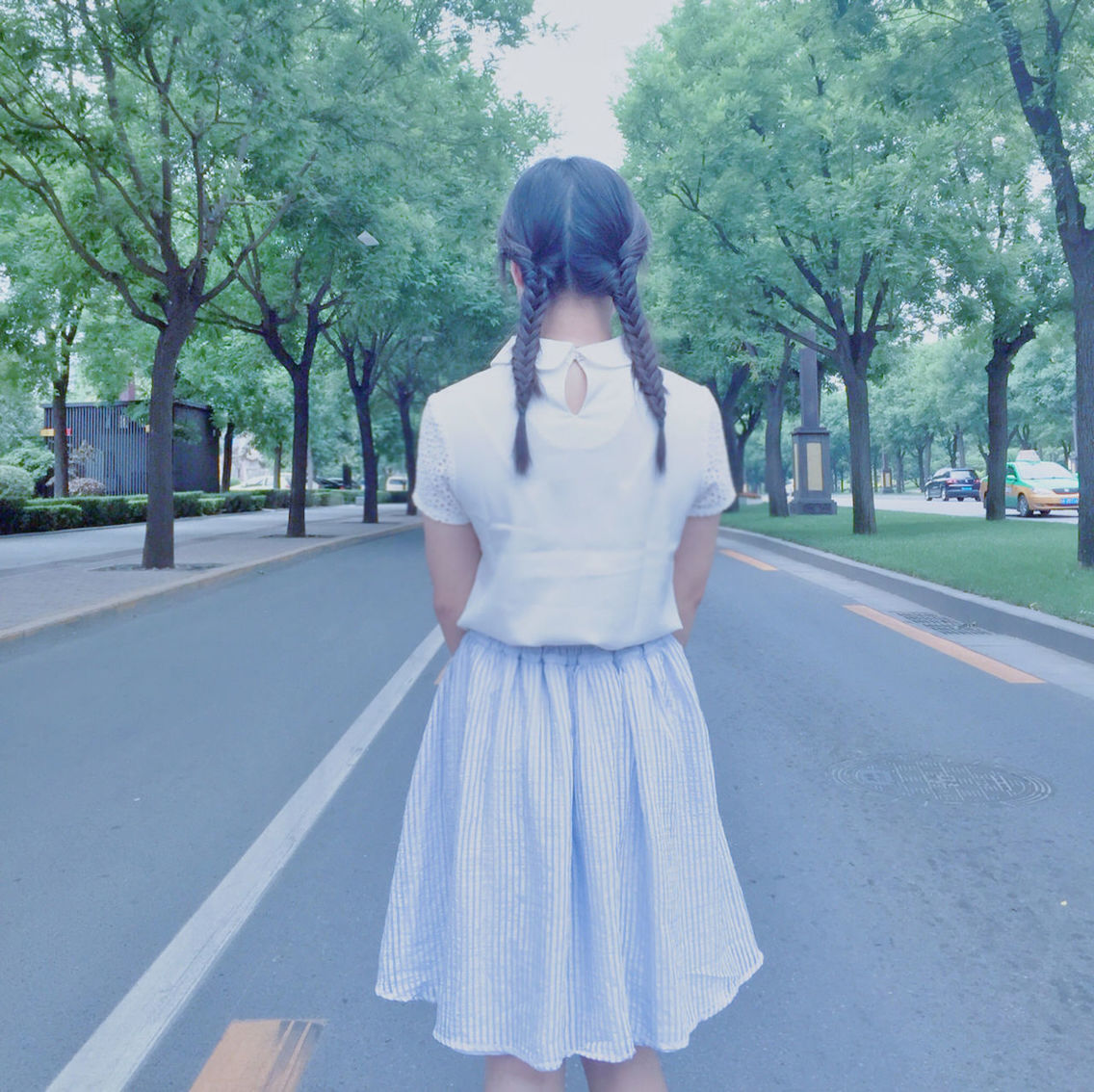 one person, tree, dress, plant, women, road, fashion, skirt, blue, standing, young adult, hairstyle, white, day, transportation, city, full length, clothing, adult, casual clothing, spring, street, nature, front view, female, lifestyles, costume, outdoors, child, long hair, leisure activity, walking, looking
