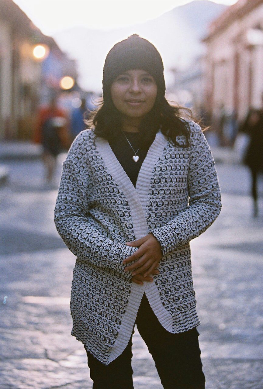 Portrait of young woman wearing warm clothing while standing on road in city
