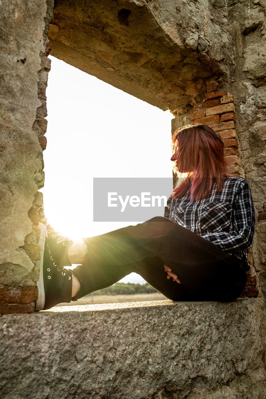 Red-haired girl sitting in a window of a building at sunset
